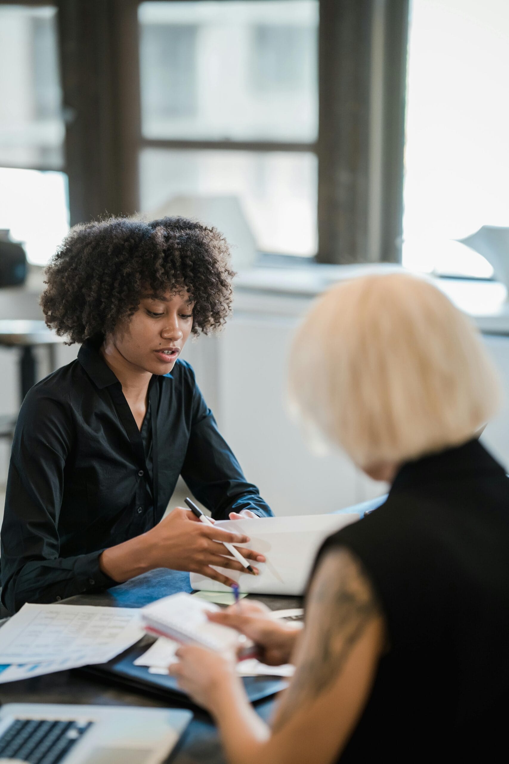 Two women discussing ideas at a table in a bright, modern office environment.